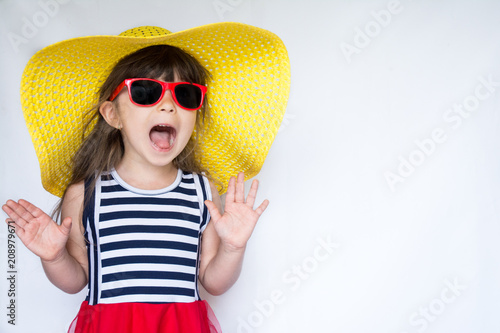Joyful surprised little girl in colorful clothes and sunglasses standing on white background. Kid's fashion. Summer holidays.