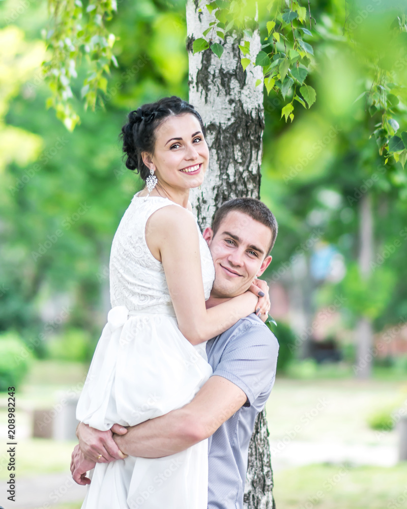 Portrait of young couple female bride and male bridegroom hugging in summer park. Man husband raised woman wife and both looking into camera. Couple in love under birch tree. Happy family smiling Portrait of young couple female bride and male bridegroom hugging in summer park. Man husband raised woman wife and both looking into camera. Couple in love under birch tree. Happy family smiling