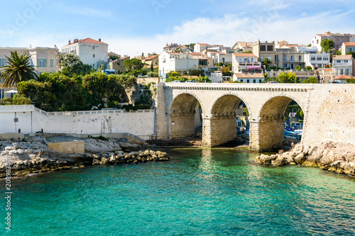 View of the bay and bridge of Fausse Monnaie (literally "counterfeit money") in Endoume district in Marseille, France, with people sunbathing on the rocks and swimming in the clear waters.