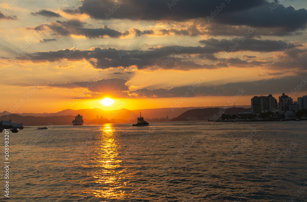 Obraz premium Cargo ship leaving the harbor, sailing out to sea with a beautiful sunset 