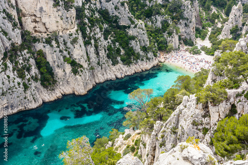 View from above of the calanque of En-Vau, a hard-to-reach narrow natural creek with white sandy beach close to Marseille and Cassis, with people sunbathing and swimming in the crystal clear water.