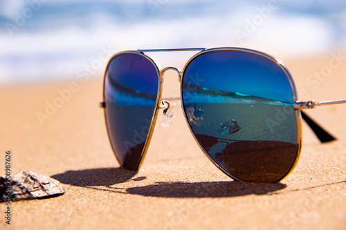 Stormy sea and shell are reflected in the mirror sunglasses on tropical beach ocean on background