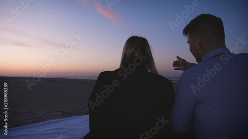 Young couple in love (guy and girl) are sitting on the sand on the sea, sunset, darkness.