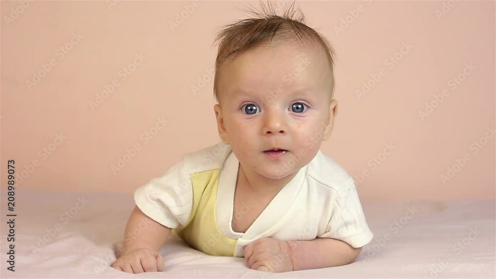 A small cute newborn boy lies on his stomach. He looks at the camera. A small cute newborn boy lies on his stomach. He looks at the camera.