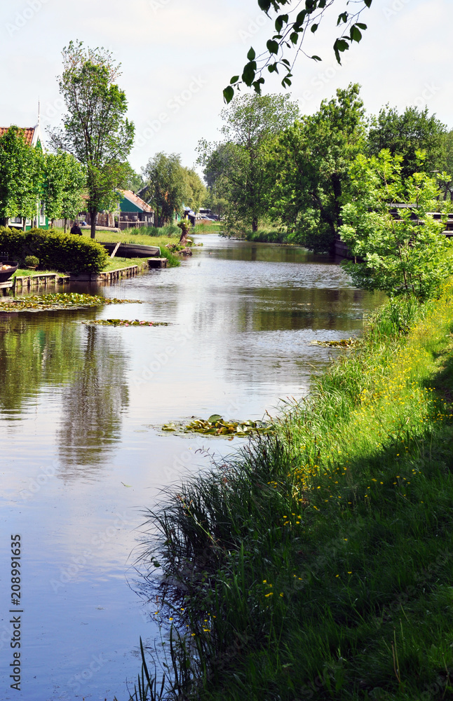 Landscape of the village in the Netherlands. The wooden houses are colourful and set along a picturesque lake surrounded by trees .