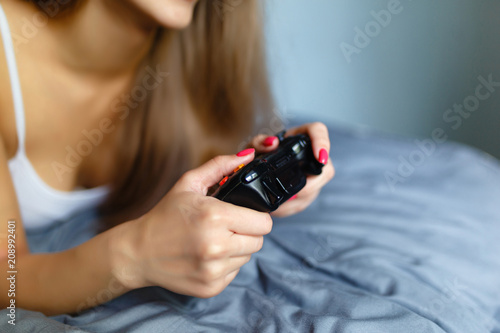 Girl gamer playing with a wireless controller, looking at the screen in front. Young girl eSports player smiling and enjoying the victory with gamepad in hand, playing video games on the console.