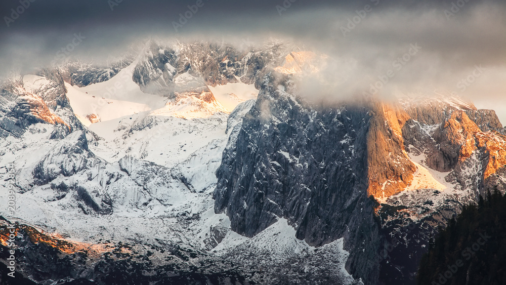 Panorama of Dachstein mountains peaks with sunset light Austria. Peaks covered with clouds
