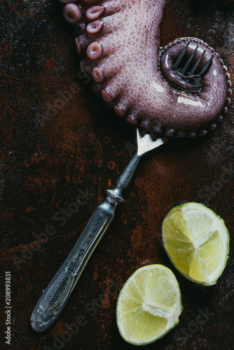 top view of big octopus tentacle with fork and limes on rusty metal surface