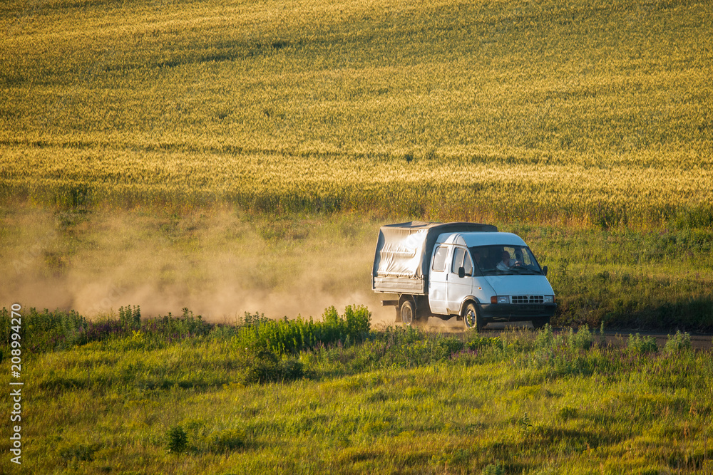 Truck drives on a dirt road and whirls a dust cloud among the fields Truck drives on a dirt road and whirls a dust cloud among the fields