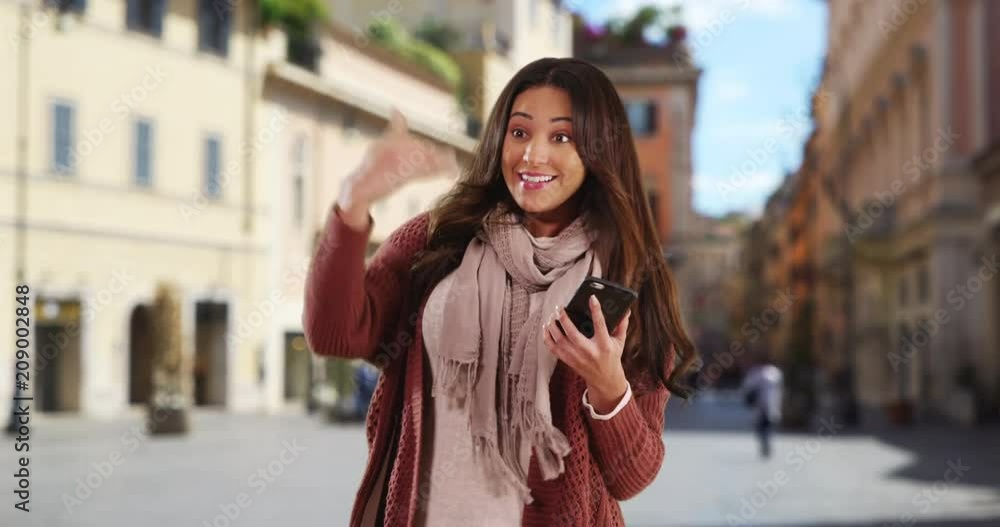 Smiling Latina woman with her phone waving to a friend, Portrait of happy attractive woman smiling and saying hi, 4k