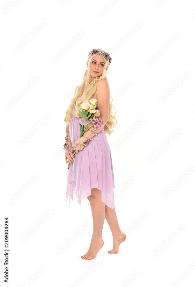 full length portrait of blonde fairy girl, holding flowers. standing pose on white studio background.