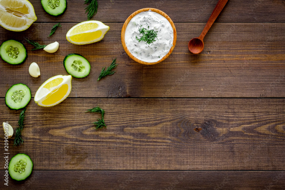 Greek yogurt dip with greenery, cucumber, oranges, garlic on dark wooden background top view space for text pattern, frame Greek yogurt dip with greenery, cucumber, oranges, garlic on dark wooden background top view space for text pattern, frame