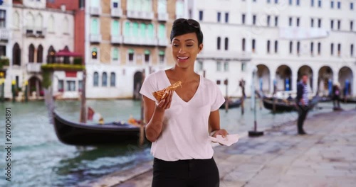 Cheerful smiling African American woman tourist in Venice, Italy eats slice of pizza, Hungry female enjoying pizza by the Grand Canal happy and laughing, 4k 