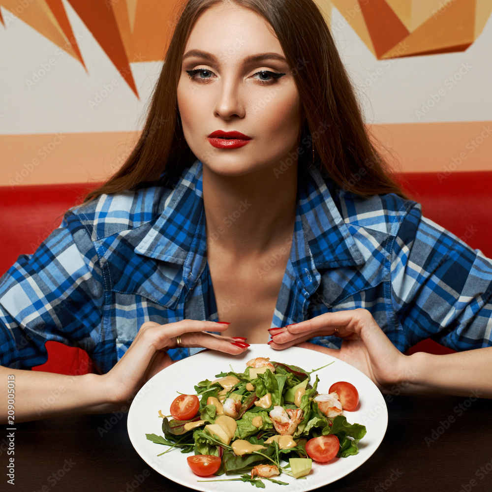 Portrait of seductive young woman dressed in checkered unbuttoned shirt holding plate with delicious vegetable salad made of shrimps, tomatoes, avocado. Sexy female model demonstrating tasty meal. Portrait of seductive young woman dressed in checkered unbuttoned shirt holding plate with delicious vegetable salad made of shrimps, tomatoes, avocado. Sexy female model demonstrating tasty meal.