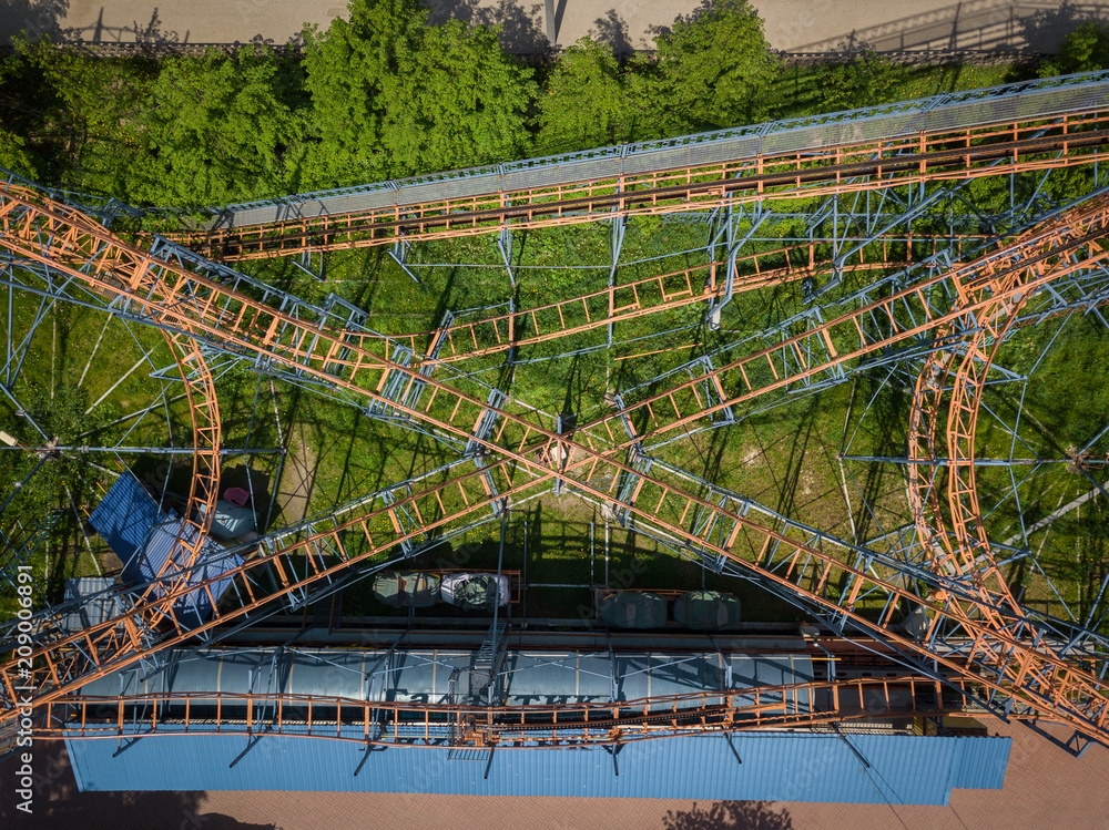 Fototapeta premium Aerial photography of a children's orange roller coaster with loops and rises in the hill in the city park on a warm summer day. Helicopter drone shot