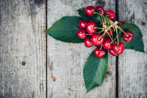 fresh red cherries on an old wooden table with green leaves, rustic style