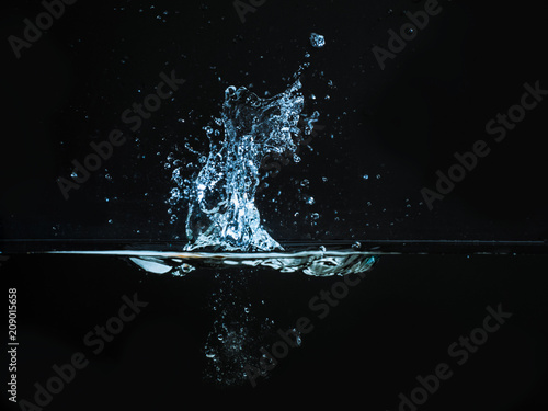 Droplet of water dropped into liquid and photographed while making splash on surface. Water splash isolated on dark background. Explosion on the water surface, abstract backgrond. Plash of liquid