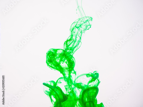 Green acrylic colour dissolving into water, close up view. Abstract green coloured background. Acrylic paint dropped into water and photographed while in motion. Droplet of color on white background