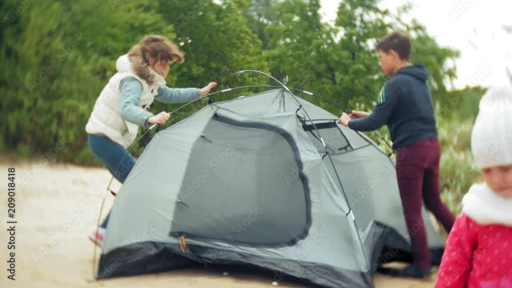 Family of children and mothers gather a tourist tent on the bank of the river of the sea Family of children and mothers gather a tourist tent on the bank of the river of the sea