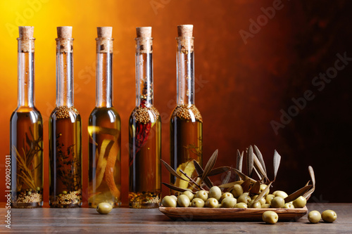 Green olives and bottles of olive oil with warious spices and herbs .