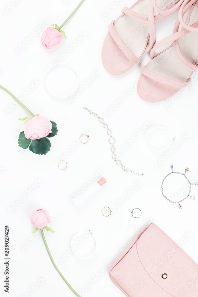 Fashion blogger workspace flat lay with sandals, jewelry, cosmetics, purse and flowers.