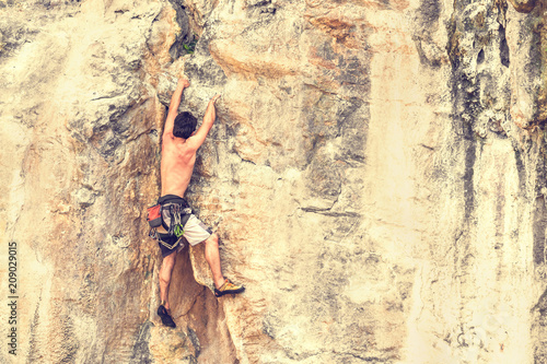 A young male climber climbs on a rock without a safety rope