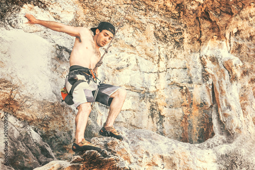 Young male climber hanging on a safety rope in the mountains. Toned