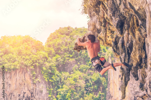 Young male climber hanging on a ledge of a cliff without safety equipment