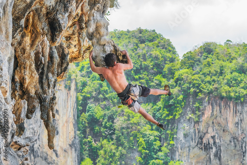 Canvas Print A young man hanging on a ledge of a cliff against the background of mountains