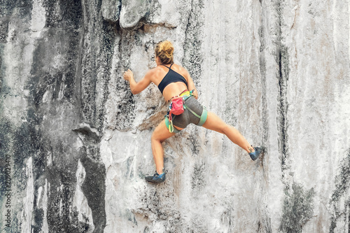 Young woman climber climbing a cliff without a tether