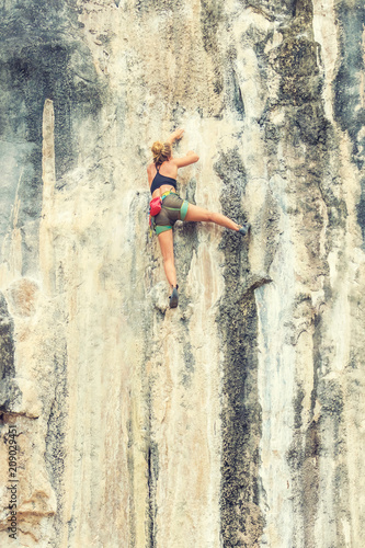 Young woman climbs a rock with a risk to life
