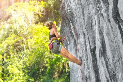 Young woman climbing a cliff with a safety rope on a sunny summer day