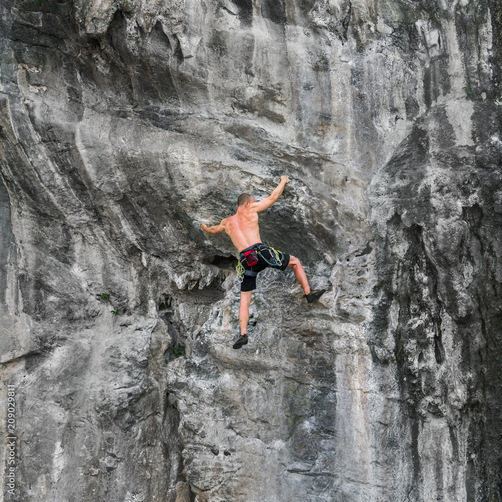 A young strong man climbs the cliff without a safety rope. Adrenaline, risk, ambition