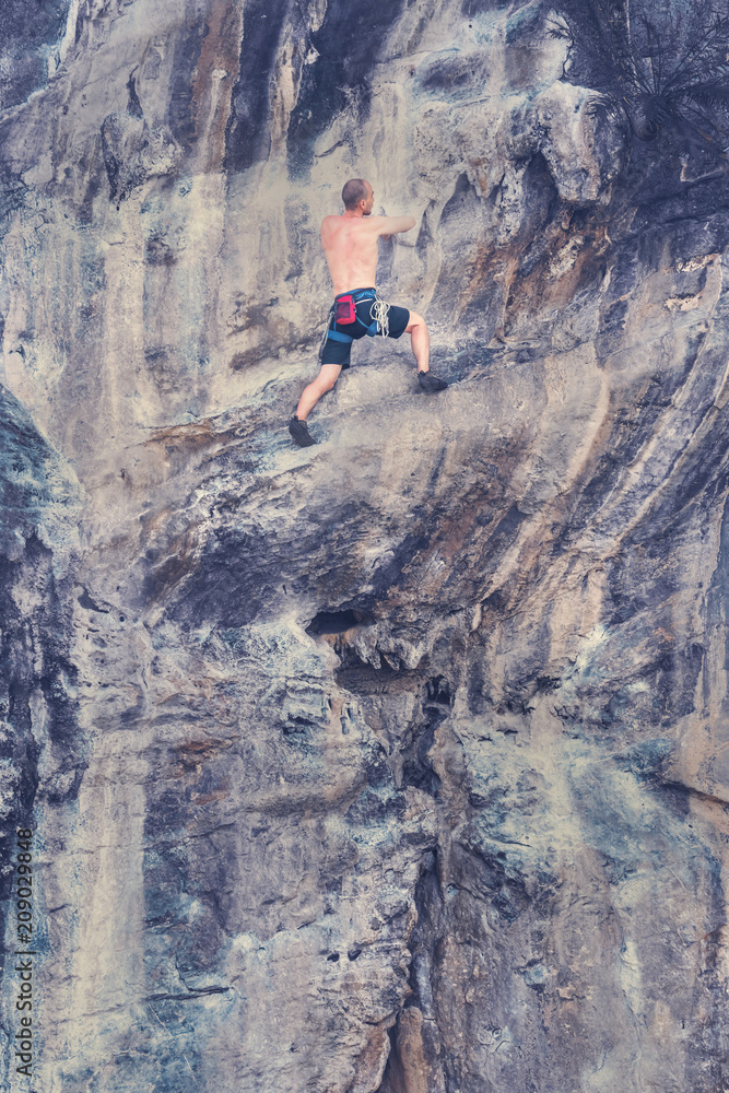 Young male climber climbing a rock wall without safety rope. Toned
