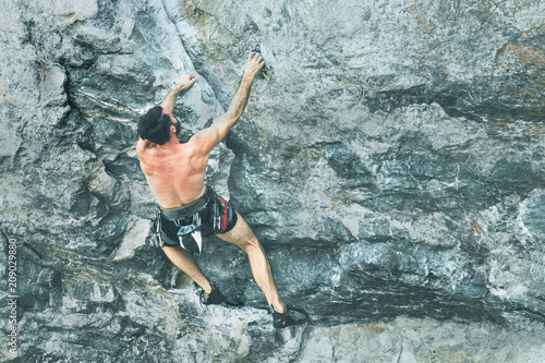 A young bearded man is climbing a rock
