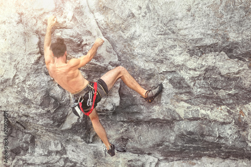 Young male climber climbing a rock wall without insurance equipment. Toned