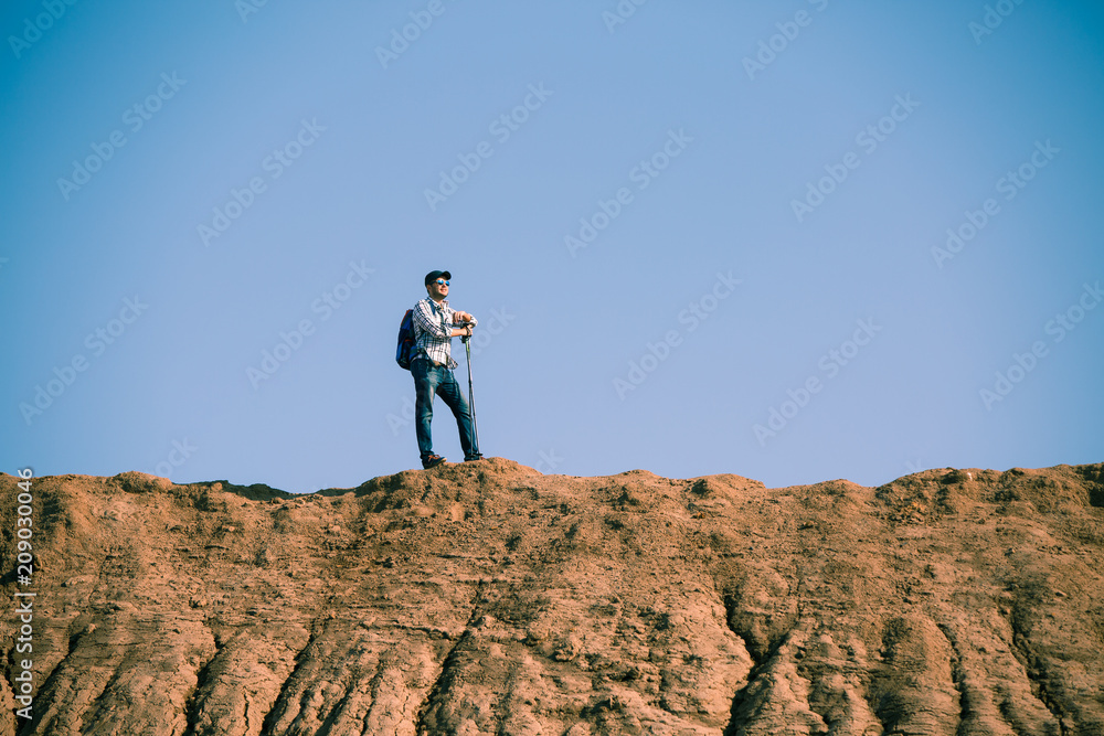 Picture of afar of tourist man with sticks for walking on hill against blue sky