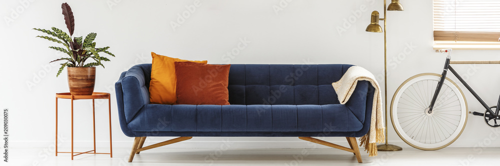 Real photo of a simple living room interior with orange cushions on a navy blue  sofa standing between a metal table and golden lamp Stock Photo | Adobe  Stock