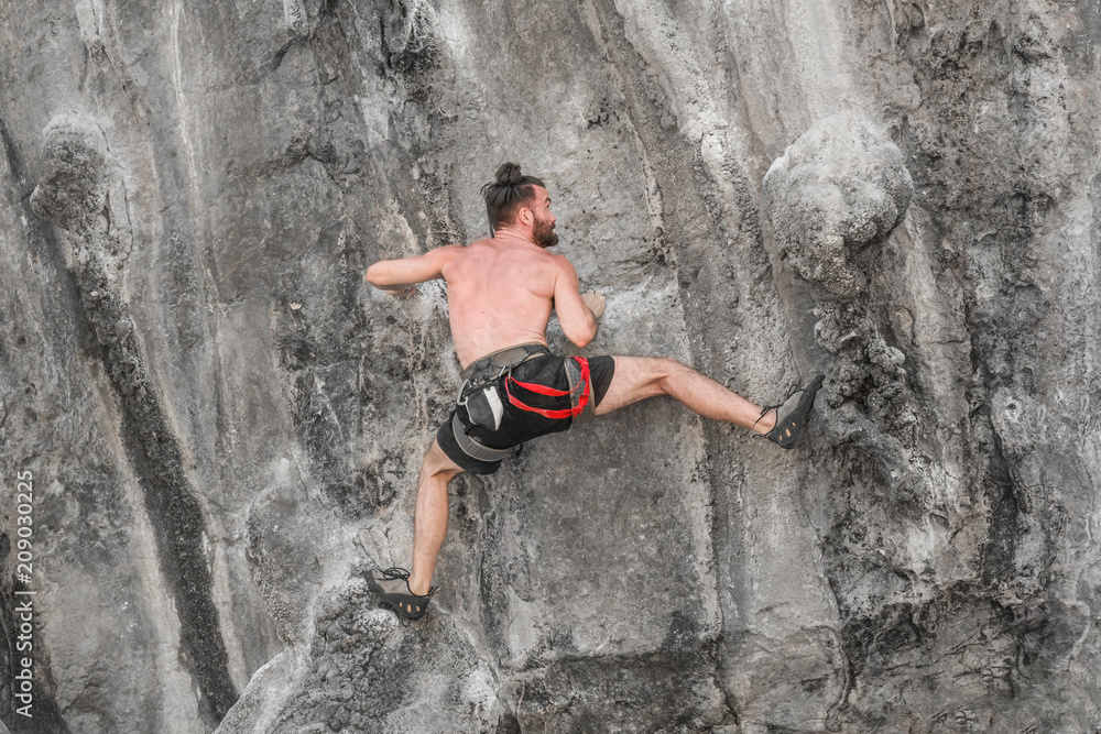 Young bearded man climbing a rock wall without  insurance equipment