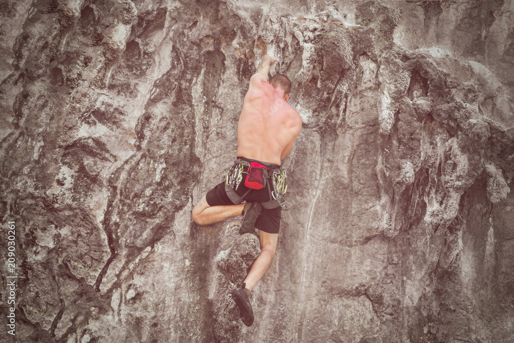 Young male climber climbing a rock wall. Toned Young male climber climbing a rock wall. Toned