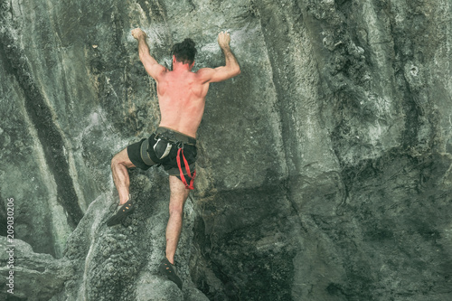 Young male mountaineer climbs on a rocky wall without rock-climbing equipment. Toned