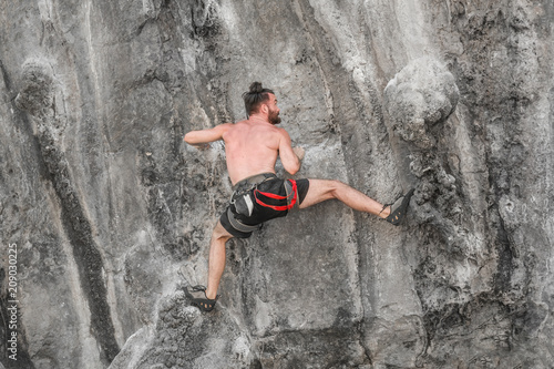 Young bearded man climbing a rock wall without insurance equipment