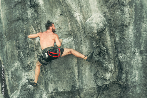 Young bearded male climber climbs the cliff