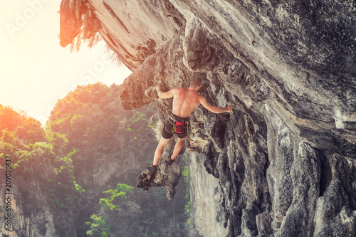 Young male climber hanging by a cliff without safety equipment on a sunny day