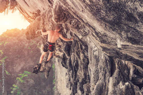 A young climber standing on a ledge of a cliff on a sunny summer day