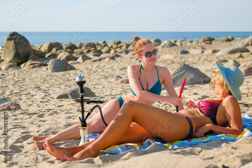 Two young girls smoking a hookah on the sandy beach