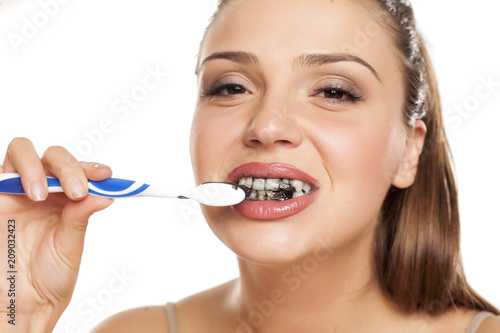 young woman brushing her teeth with black toothpaste of activated charcoal on white background