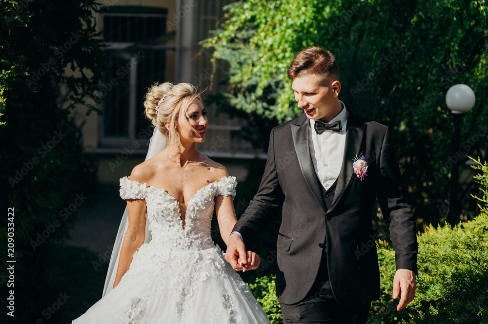 Amazing smiling wedding couple. Pretty bride and stylish groom. Wedding photo outdoor. White dress and black suit. Kisses of a smile.