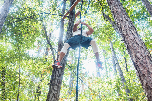 Fit man climbing rope high up in outdoor gym