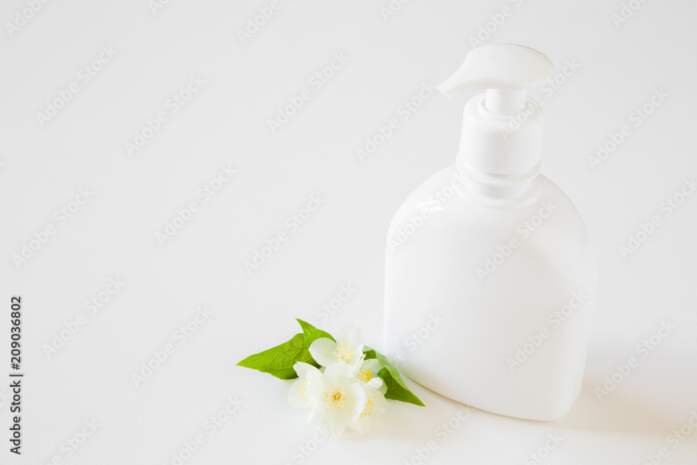White bottle of natural herbal cream for women on gray table. Beautiful jasmine blossoms. Fresh flowers. Care about clean and soft face, hands, legs and body skin. Empty place for text or logo. White bottle of natural herbal cream for women on gray table. Beautiful jasmine blossoms. Fresh flowers. Care about clean and soft face, hands, legs and body skin. Empty place for text or logo.